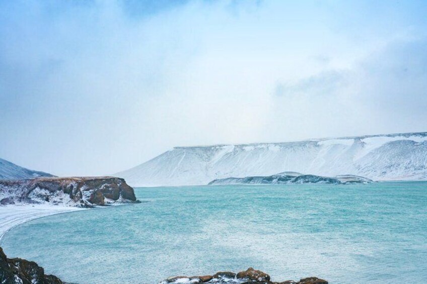 A coastal landscape with a snow-covered cliff and calm turquoise waters. 5