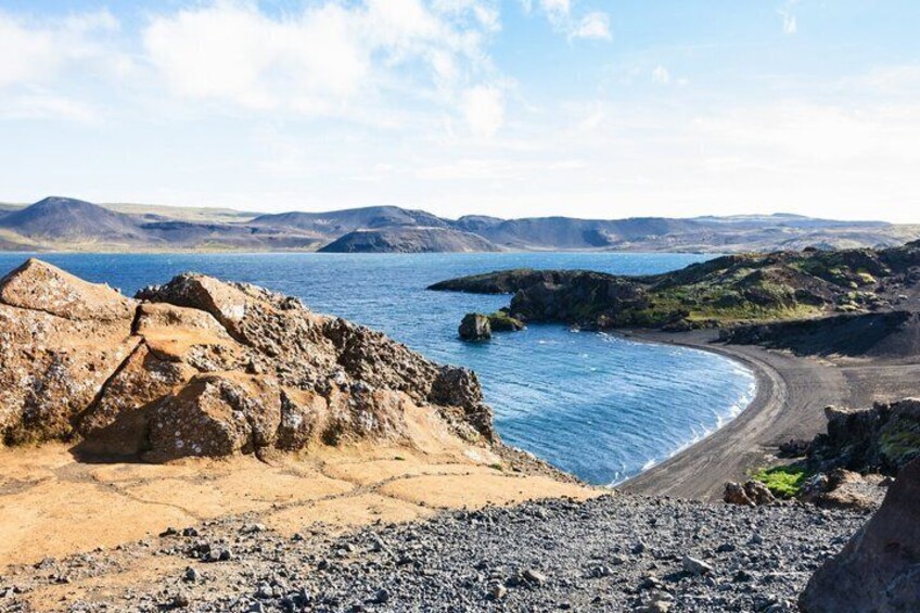 A coastal landscape with rocky terrain, a sandy beach, and a calm sea. 4