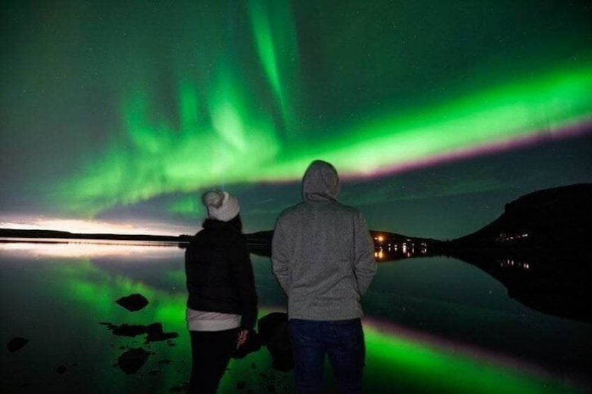 Two people observing the Northern Lights over a calm body of water. 1