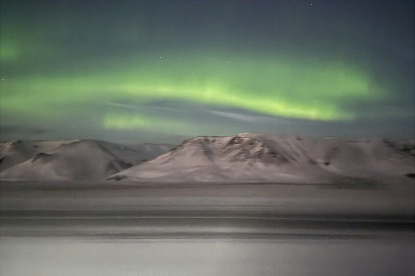 A snowy mountain range with a calm body of water in the foreground and the aurora borealis in the sky. 3