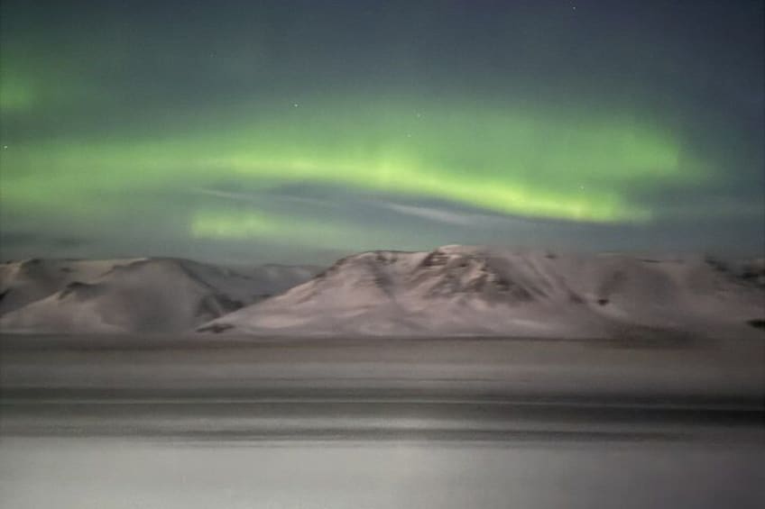 A snowy mountain range with a calm body of water in the foreground and the aurora borealis in the sky. 3
