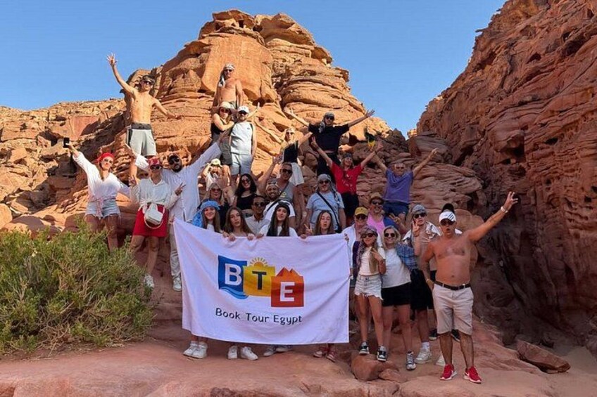 A group of people posing in a rocky canyon with a banner reading 'Book Tour Egypt.' 2