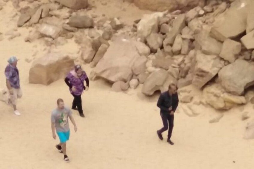 A sandy beach with large rocks and people walking. 4