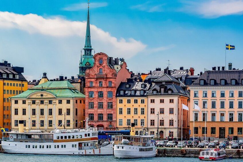 A waterfront cityscape with colorful buildings, a prominent church spire, and a Swedish flag. 4