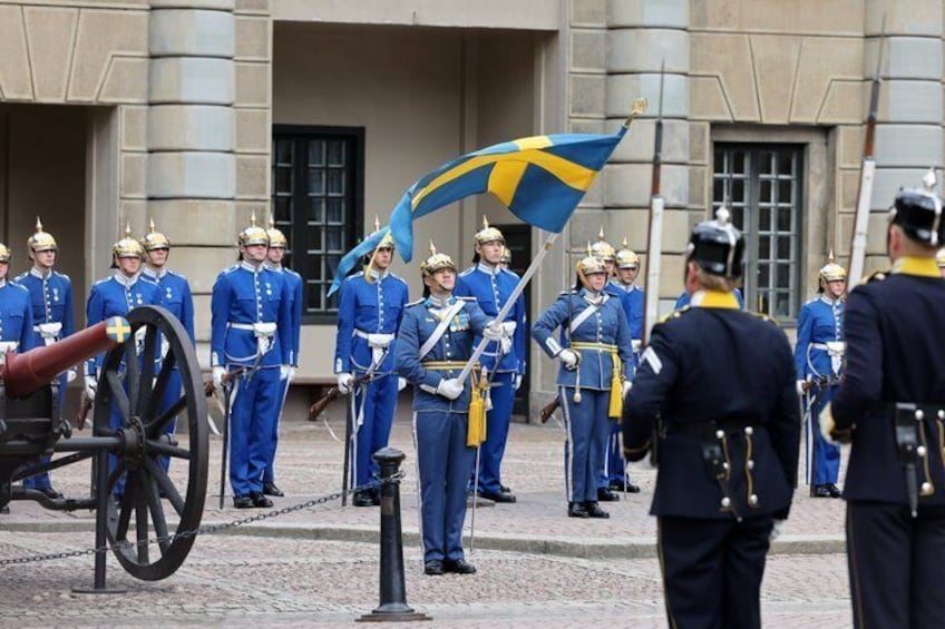A ceremonial guard in blue uniforms with a flag, standing in front of a building with columns. 2