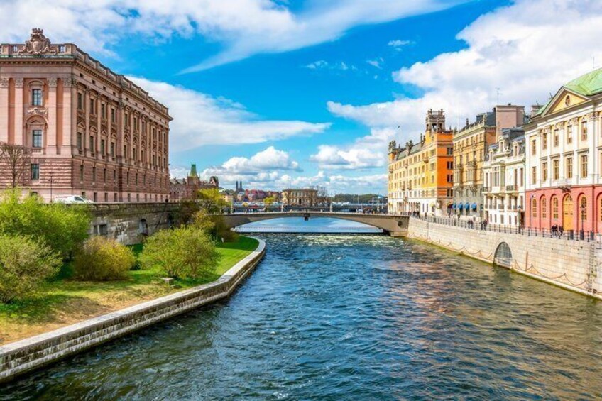 A river with buildings on either side, a bridge in the distance, and a clear blue sky. 1