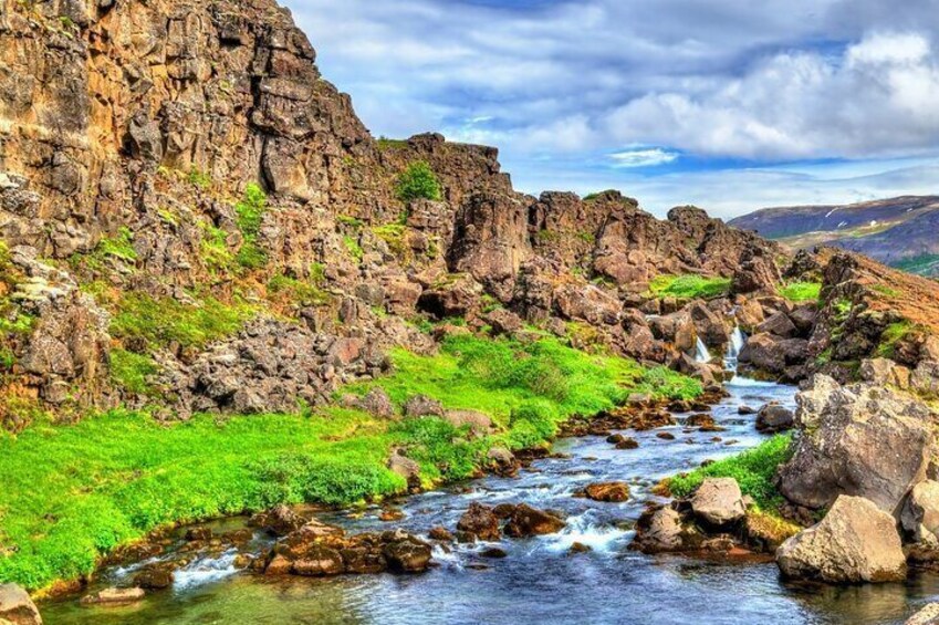 A river flowing through a rocky landscape with green vegetation and a mountainous backdrop. 2