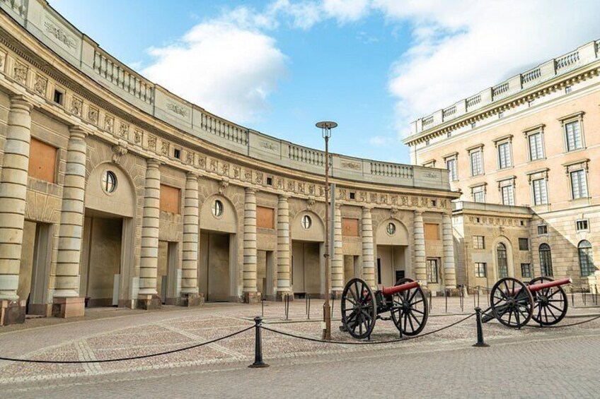A historic building with a curved facade, a central column, and two red cannon on display. 2