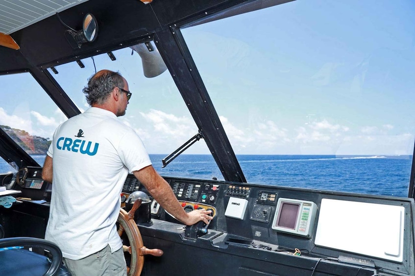 A man in a white shirt with "CREW" on the back, steering a boat. 3