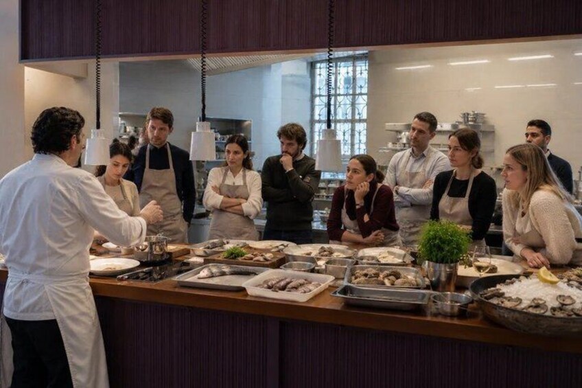 A group of people in a kitchen, some wearing aprons, with food items on the counter. 5