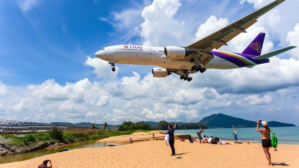 A Thai Airways airplane landing on a beach with people and a river in the background. 1