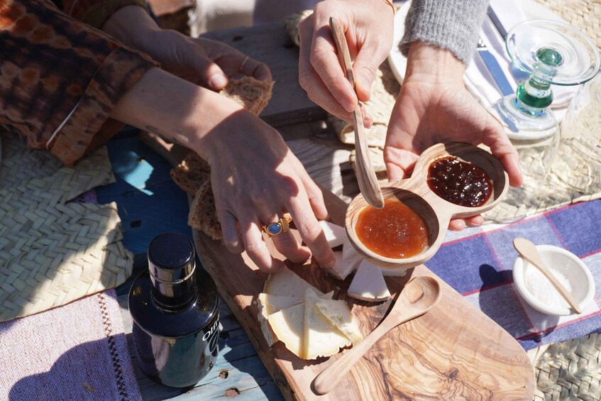Hands spreading jam on cheese slices, a bottle, and wooden bowls on a woven mat. 5