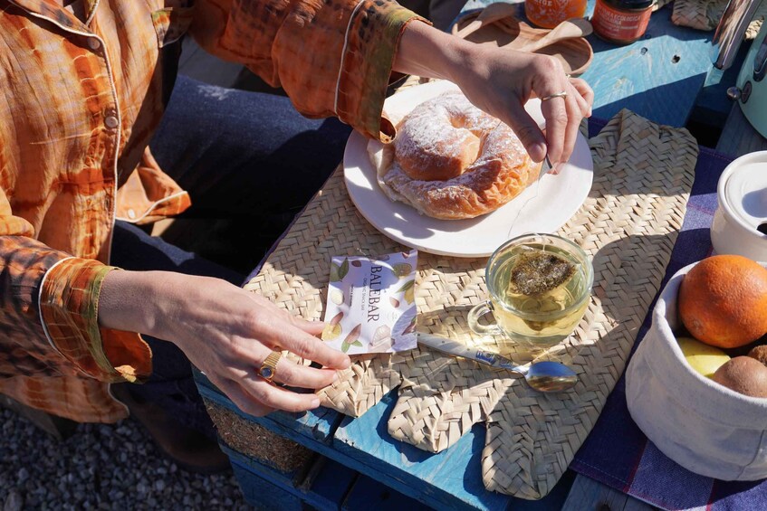 A person serving a pastry on a plate, a glass of white wine, and a basket of oranges on a table. 2