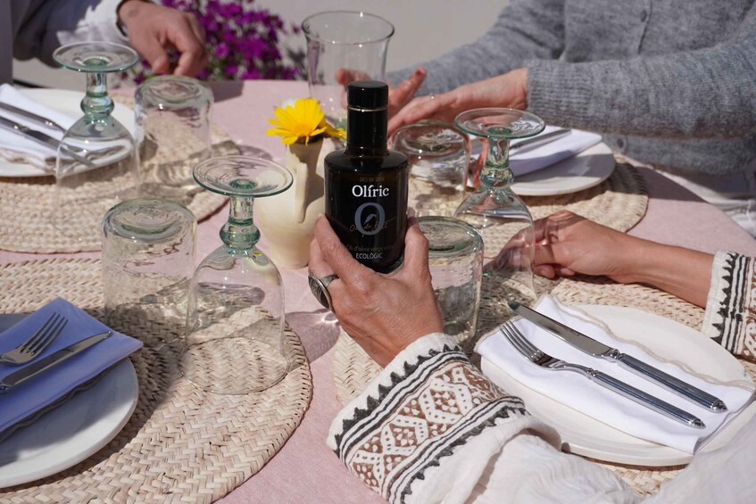 A table set with glassware, a bottle of Olfric olive oil, and a yellow flower. 4