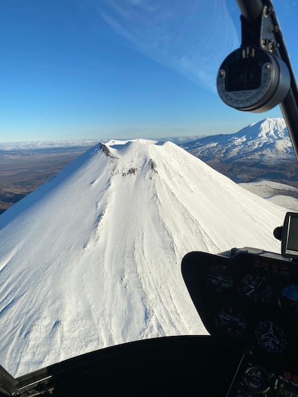 A snow-covered mountain peak from an aircraft cockpit, with a clear sky and distant landscape. 3