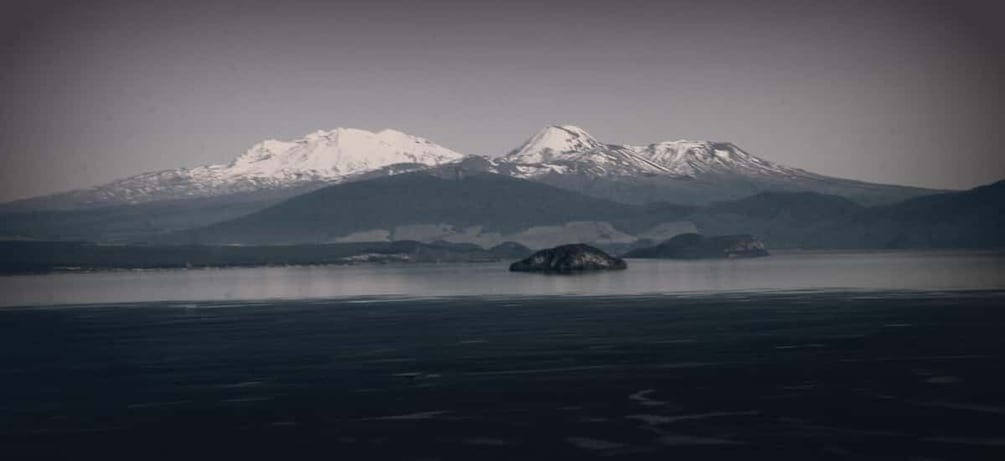A mountain range with snow-capped peaks and a calm body of water with an island in the foreground. 5