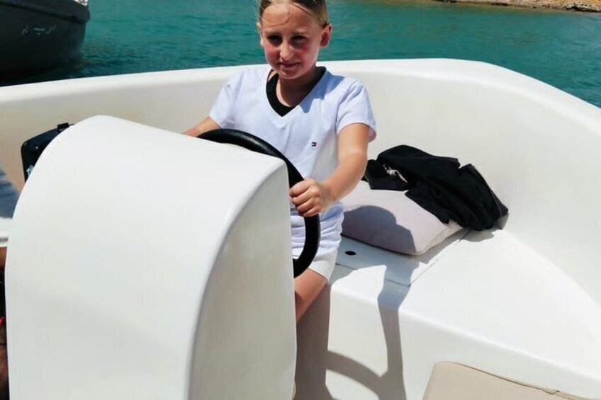 A person in a boat steering, with a white boat and calm water in the background. 2