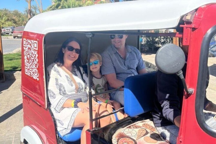 A red auto-rickshaw with a QR code on the back, passengers inside, and a blue seat visible. 1