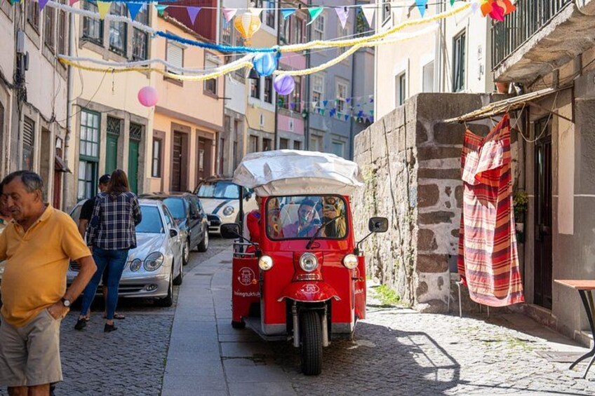 A narrow street with a red vintage car, pedestrians, and buildings. 4