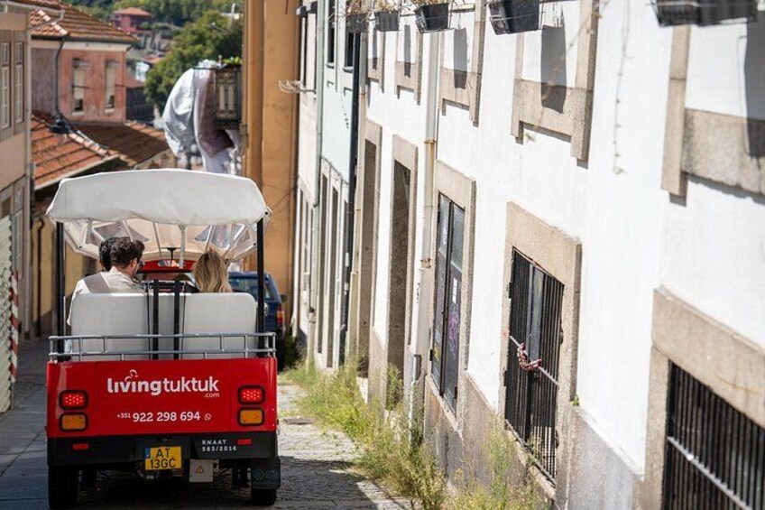 A red vehicle with a white canopy driving down a narrow street. 5