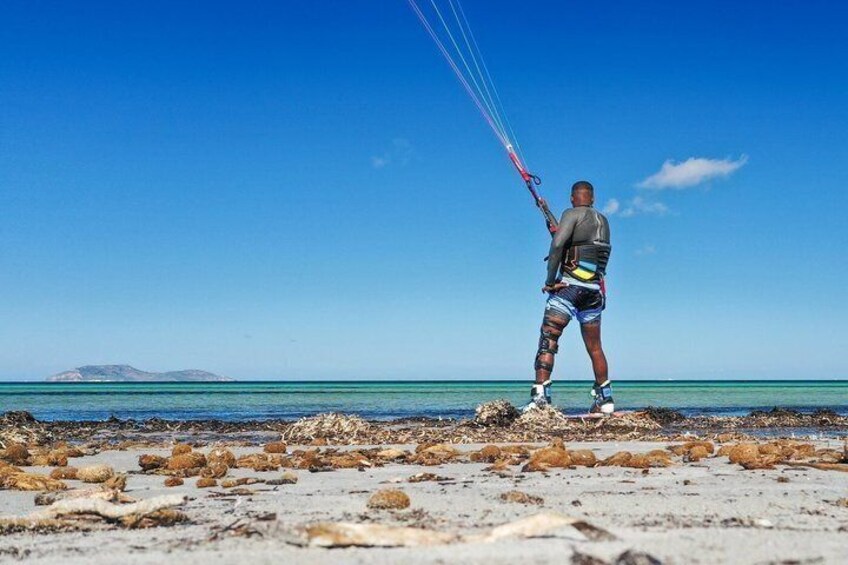A person kite surfing on a beach with clear blue water and a distant island. 5