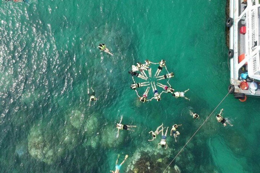 A group of people swimming in a circular formation in clear turquoise water. 1