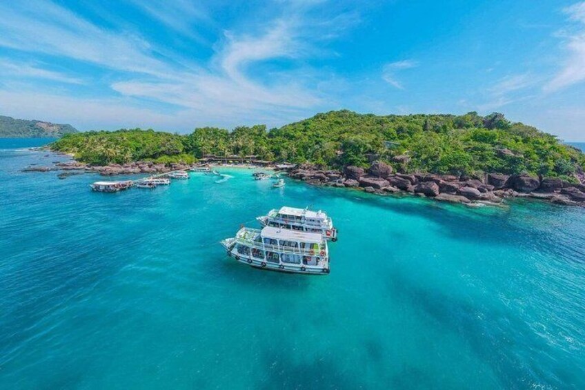 A boat in turquoise waters surrounded by a rocky island with lush greenery. 4