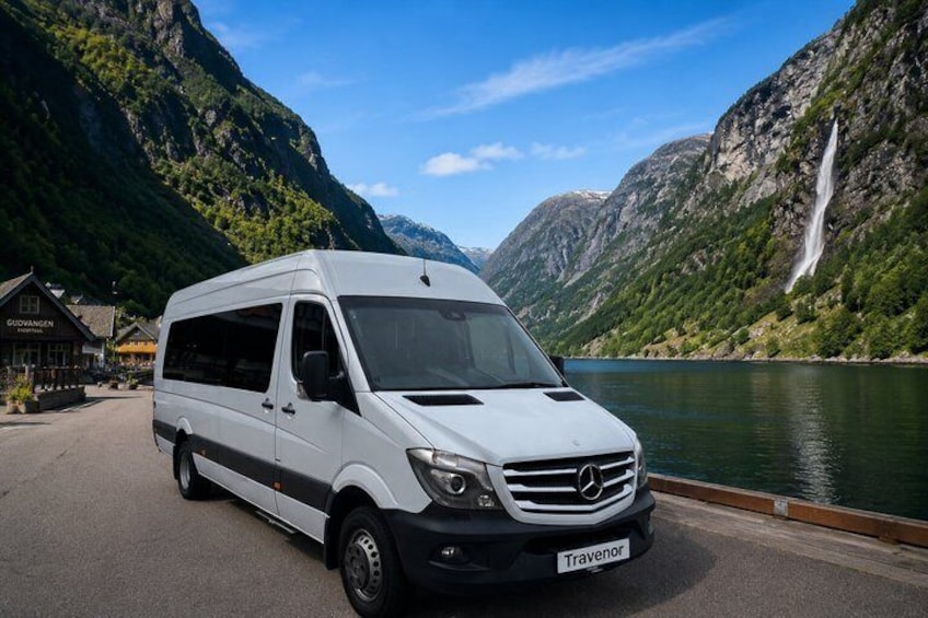 A white Mercedes van parked by a lake with mountains in the background. 2