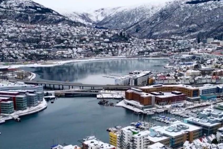 A coastal city with a marina, buildings, and snow-covered mountains. 1