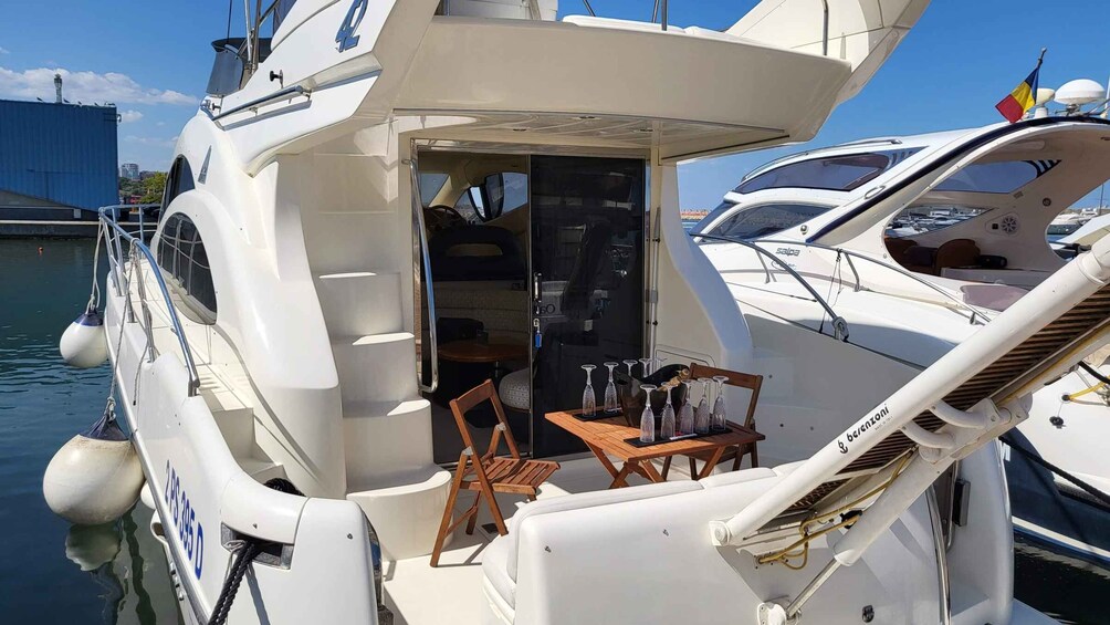 A yacht docked at a marina with a small table and chairs on deck. 3