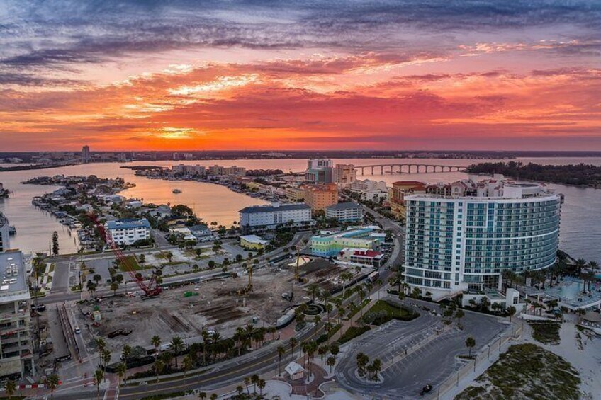 A waterfront cityscape at sunset with a bridge, a large hotel, and a marina. 4