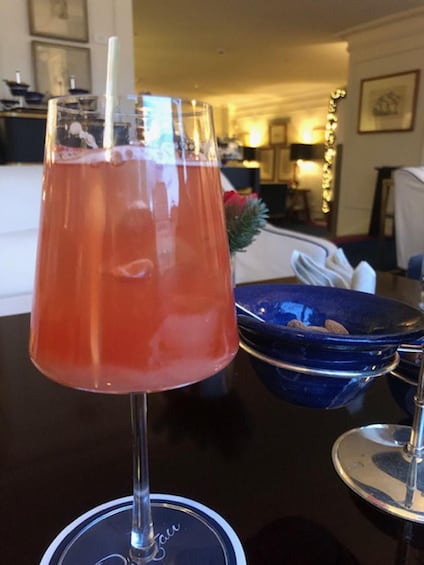 A cocktail glass with a straw on a coaster, a blue bowl with nuts, and a blurred background of a room with a Christmas tree. 1