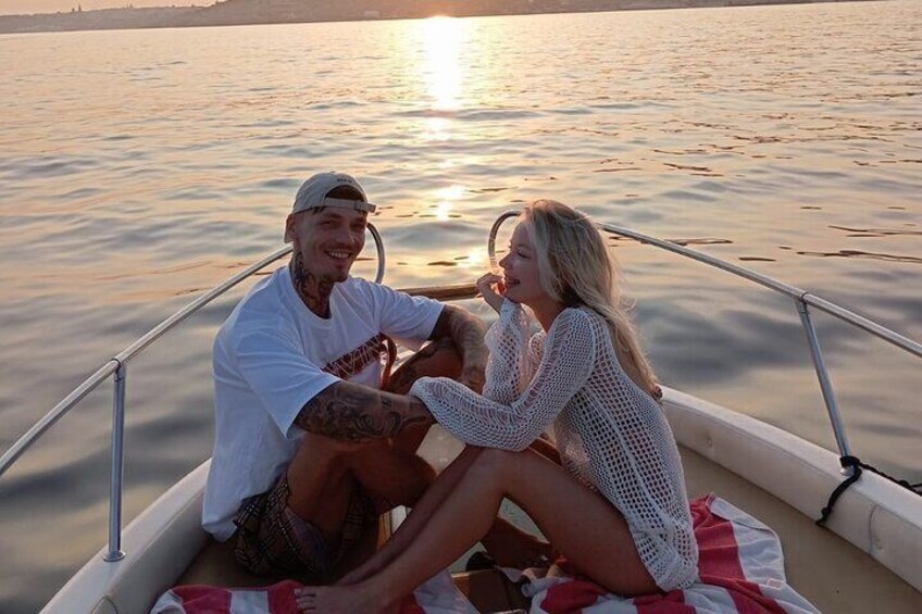 Two people on a boat with a calm water body and a sunset in the background. 3