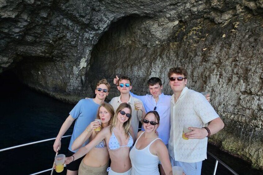 A group of people on a boat near a rocky cave entrance. 1