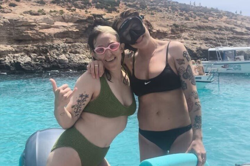 Two people in swimwear by a clear blue sea with rocky cliffs in the background. 5