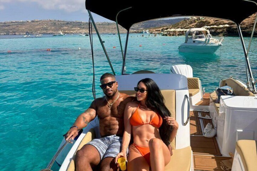 A couple on a boat in clear blue waters with a rocky coastline in the background. 1