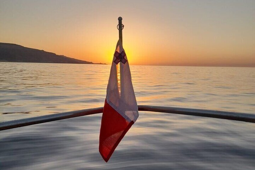 A sunset over calm waters with a flag hanging from a boat's railing. 2