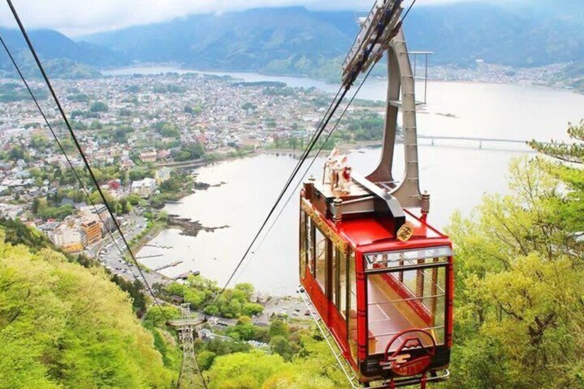 A red cable car suspended over a river, with a cityscape and mountains in the background. 1