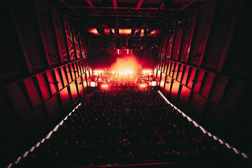 An indoor concert venue with rows of seats, a stage with lighting, and a crowd. 5