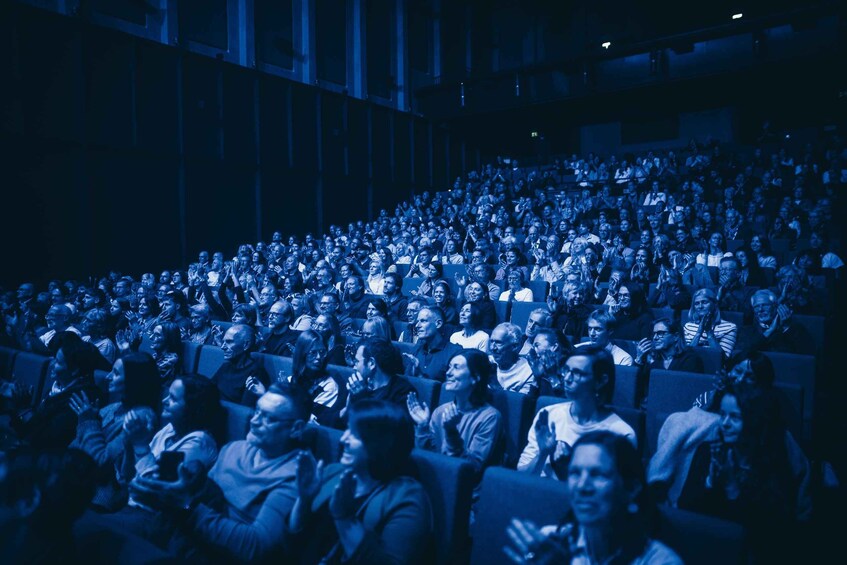 An indoor auditorium filled with seated audience members. 2