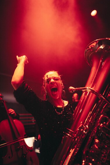 A person playing a brass instrument, likely a tuba, in a dimly lit setting with red lighting. 3
