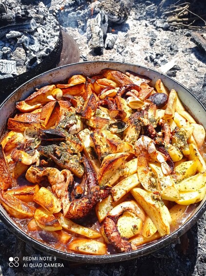 A pan of roasted potatoes and octopus seasoned with herbs, cooked over an open fire. 2