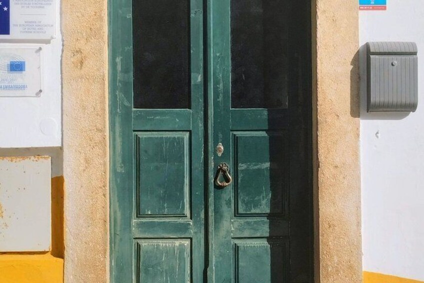 A green door with a metal handle and a keyhole, a utility box on the wall, and a sign with text. 2