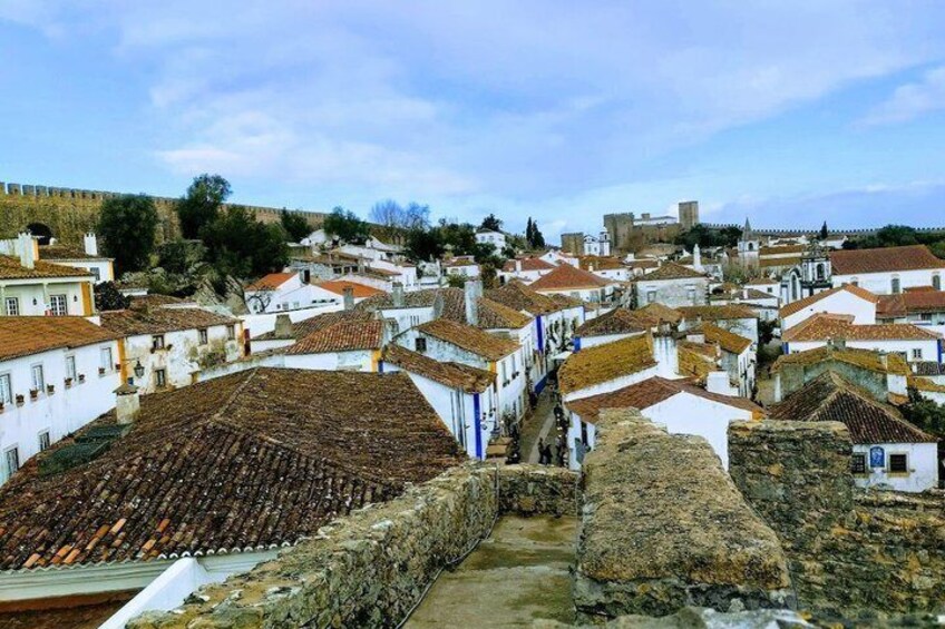 A historic town with white buildings and terracotta roofs, a stone wall, and a hill in the background. 5