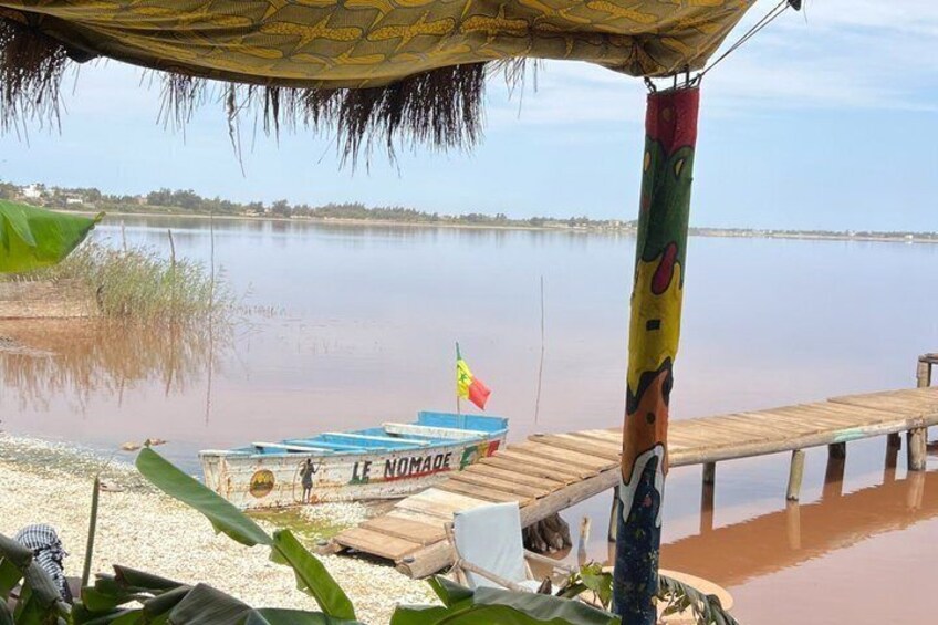 A wooden dock extending into a calm body of water, a small boat named 'Le Nomade' with a flag, and a colorful pole with a face design. 2