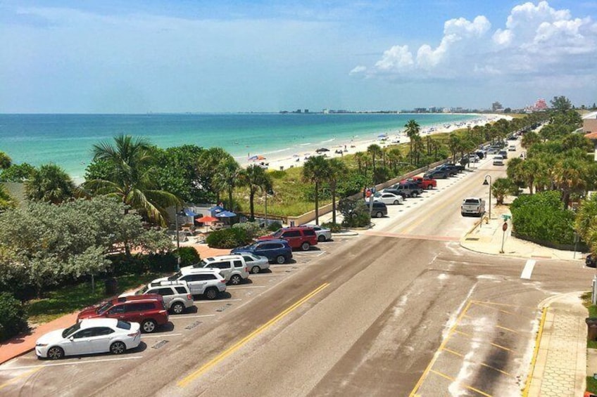 A coastal road with parked cars, a beach, and palm trees. 5