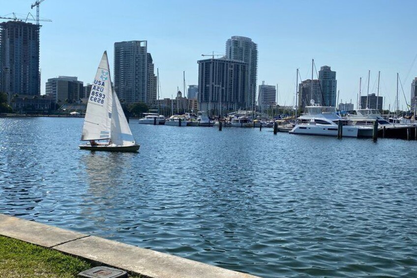 A sailboat on a calm river with a city skyline in the background. 3