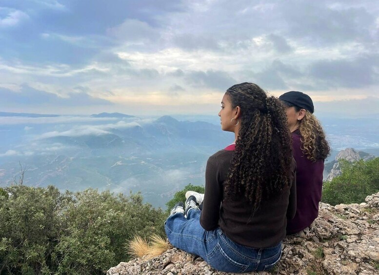 Two individuals sitting on a rocky outcrop overlooking a mountainous landscape. 4