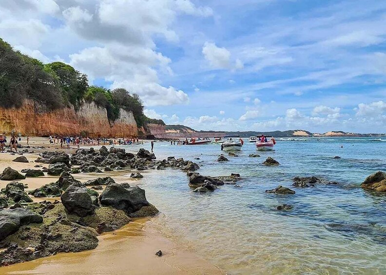 A rocky beach with clear water, people walking, and boats in the distance. 5