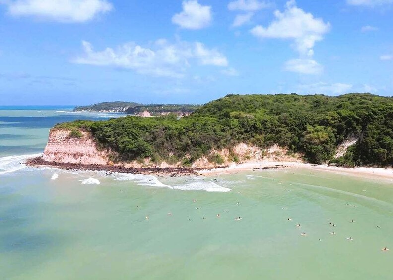 A coastal landscape with a sandy beach, clear turquoise waters, and a green hill with dense vegetation. 1